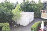 Vista de pássaro sobre uma garagem dupla independente com telhado plano num pátio pavimentado rodeado por arbustos e bicicletas