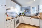 Innenansicht einer L-förmigen Wohnungsküche in Weiß mit Holzarbeitsplatte und blau gemusterter Fliesenrückwand