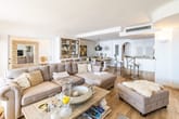 helle offene Wohnraumansicht von Wohnzimmer mit hellem Parkett, Ecksofa, Couchtisch und Bartresen