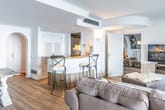 Innenraum moderne Wohnung aus Wohnzimmerperspektive mit offener Bartheke, Holzfußboden, Sofalandschaft und Zugang zum Nebenraum