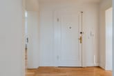 Innenflur einer Wohnung mit weißer Eingangstür, Parkettboden und zwei offenen Zimmertüren
