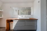 Innenaufnahme modernes Badezimmer mit grauem Waschtischunterschrank und Holzarbeitsplatte Spiegel und Dusche im Hintergrund