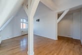 Dachgeschosswohnung Innenansicht mit offenem Wohnraum sichtbaren weißen Dachbalken Holzboden und Sprossenfenster