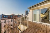 Blick von Dachterrasse einer Penthousewohnung auf Holzdielen, umlaufendes Metallgeländer und bodentiefe Glas-Schiebetüren