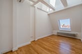 Innenansicht eines leeren Dachgeschosszimmers mit Holzparkett, Dachfenster, Deckenbalken und Wandheizkörper