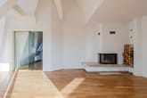 Innenansicht eines hellen Dachgeschoss-Lofts mit Parkettboden, Glas-Schiebetür und Kamin mit Holzfach