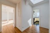 Blick von Flur einer Dachgeschosswohnung auf Wohnzimmer mit Stützbalken und Küche mit Dachfenster