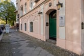 Schrägansicht Altbauwohnhaus-Fassade mit rosafarbenem Putz gewölbten Fensterbögen grünem Hauseingang und Laterne