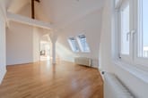 Innenansicht einer hellen Dachgeschosswohnung mit offenem Grundriss Parkettboden sichtbaren Holzbalken und zwei Dachfenstern