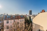 Aus erhöhter Perspektive Blick auf dreigeschossiges Altbauwohnhaus mit Gaubendach und kahlem Herbstbaum vor Hochhausbaustelle