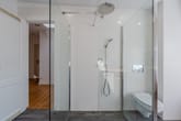 Innenansicht modernes Badezimmer mit bodengleicher Glasdusche Regen und Handbrause wandhängendem WC