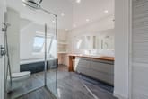 Dachgeschossbadezimmer mit begehbarer Glasdusche, Badewanne unter Dachfenster und Doppelwaschtisch mit Holzablage