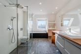 Dachgeschossbad im Neubau mit Walk-in Dusche, freistehender Badewanne unter Dachfenster und Holzwaschtisch mit Spiegel