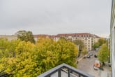 Blick von Balkon auf herbstliche Baumkronen und historische Altbaufassade einer Straßenecke mit Kopfsteinpflaster