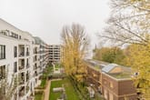 Vogelperspektive auf weißen Mehrfamilienhäusern mit Balkonen und begrüntem Innenhof neben einem niedrigen Klinkerbau