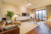 Modern eingerichtetes Wohnzimmer in Stadtwohnung mit Ledersofa, zwei Sesseln, Teppichboden und bodentiefem Balkonfenster