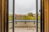 Innenblick auf Balkon einer Etagenwohnung mit Fliesenboden Metallgeländer und herbstlichen Baumkronen im Hintergrund