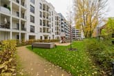 Innenhofansicht moderner Mehrfamilienhaus mit Balkonen Spielplatz Rasenfläche und Baumreihe aus schräger Perspektive