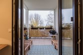 Blick durch geöffnete Wohnzimmertür auf überdachten Balkon mit Holzgartenmöbeln und bepflanztem Geländer