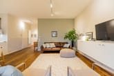 Innenansicht modernes Wohnzimmer mit Ledercouch, TV-Sideboard, Parkettboden und Zimmerpflanze aus Flurperspektive