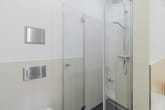 Moderner Duschbereich mit Glasabtrennung und Regenduschkopf in weiß kachelverkleidetem Bad