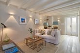 Wohnzimmer mit sichtbarer Balkendecke, weißem Sofa, verschachteltem Holztisch und Glas-Doppeltür