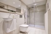modernes innenbadezimmer mit wandhängendem wc kleines waschbecken und rahmenloser glasdusche aus schräger sicht