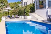 Blick auf Pool mit Sonnenschirmen und Sonnenliegen vor moderner weißer Villa mit Balkon und Terrasse