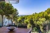 Terrassenansicht einer Meerblickvilla mit Glasgeländer und Holztisch und Blick über Pinienwald