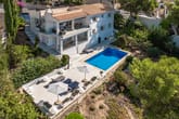 Vista aérea de villa blanca con piscina, terraza grande, sombrillas, balcón, escalera de caracol y jardín mediterráneo.