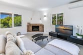 Innenansicht eines modernen Wohnzimmers mit Backsteinkamin, Ecksofa, Panoramafenstern mit Grünblick und TV-Sideboard