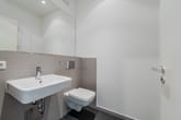 Innenansicht modernes Gäste-WC mit wandhängendem Waschbecken und Toilette vor großem Spiegel