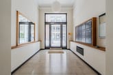 heller Flur eines Mehrfamilienhauses mit Glastür zur Straße, Briefkastenwand rechts und Spiegelwand links