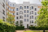 Innenhofansicht mehrstöckiges Wohnhaus mit weißer Putzfassade Klinkerakzenten und begrüntem Vorgarten