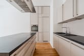 Frontale Sicht auf Küchenbereich einer Neubauwohnung mit Kochinsel, weißen Hochglanzfronten und Parkettboden