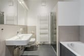 Innenansicht eines modernen Badezimmers mit Badewanne, Glasdusche, Wandwaschbecken, Toilette und Handtuchheizkörper