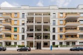 Fünfgeschossiges Mehrfamilienhaus mit weißer Putz- und gelber Klinkerfassade und Balkonreihen in Straßenansicht