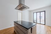 Moderne offene Wohnküche aus Frontperspektive mit Kochinsel, Induktionsfeld, Edelstahlhaube und Balkon vor Klinkerfassade
