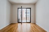 Innenansicht Neubauwohnung mit Parkettboden und bodentiefer Glastür zum Balkon