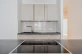 Moderne Einbauküche in Neubauwohnung mit Kochinsel Cerankochfeld und Hochglanzschränken aus Frontalperspektive