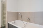 Innenansicht modernes Badezimmer mit eingelassener Wanne Handbrause Glasduschabtrennung und halbhohen beigen Fliesen