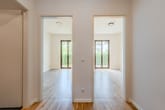Blick durch Flur auf zwei lichthelle Räume mit Parkettboden und bodentiefen Fenstertüren zum Garten