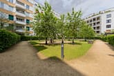 Blick in den begrünten Innenhof eines Mehrfamilienhauses mit Spielplatz, Spazierweg und umlaufenden Balkonen