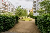 Innenhof moderner Mehrfamilienhäuser mit Rundbalkonen, hellen Fassaden und begrünten Gehwegen