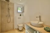 Modernes Bad Innenansicht mit bodengleicher Regenbrause Wand WC ovaler Aufsatzwaschbecken Natursteinplatte kleines Fenster