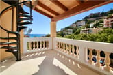 Vista desde el balcón de una villa con escalera de caracol negra, barandilla blanca, vigas de madera en el techo y vista al mar