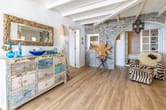 Offener Wohnbereich in Landhausstil aus Frontperspektive mit Steinwand, rustikaler Kommode, Sessel und Holzbalkendecke