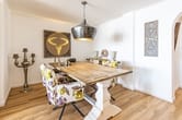 Innenansicht Esszimmer mit rustikalem Holztisch, gemusterten Polsterstühlen, hängender Metalllampe und dekorativem Wandbild