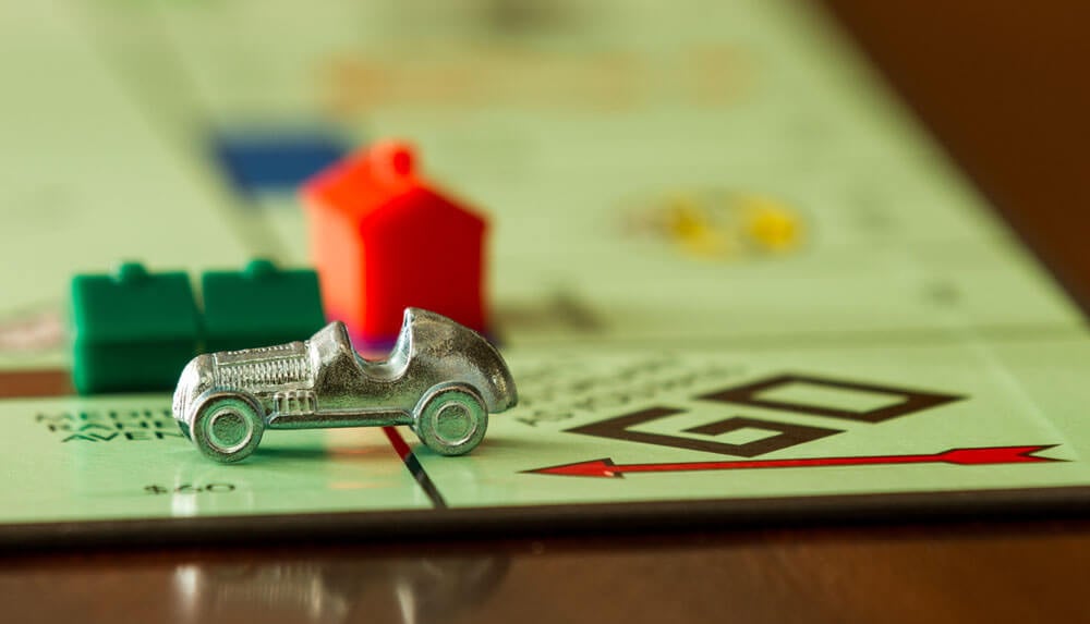 Gros plan sur un plateau de Monopoly avec une figurine de voiture argentée et des maisons rouges et vertes sur la case 50