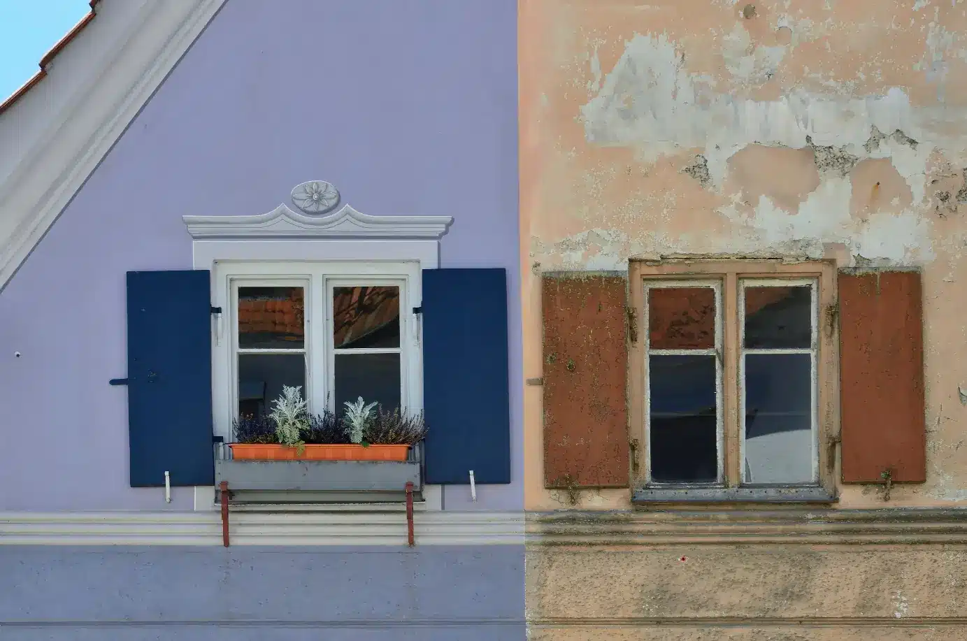Frontalansicht zweier Wohnhausfassaden mit Fenstern und Klappläden links mit Blumenkasten rechts abblätternder Putz